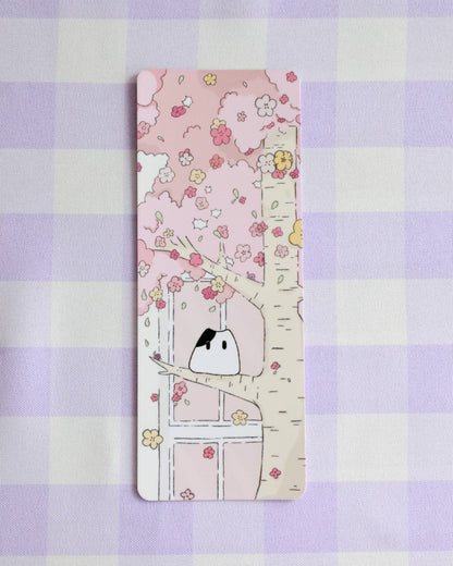 Bookmark with a cute illustration of a cat under a cherry blossom tree on a purple checkered background.