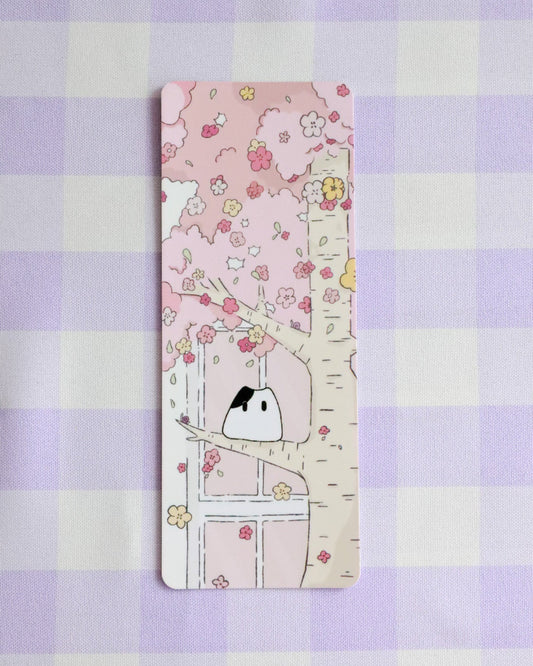 Bookmark with a cute illustration of a cat under a cherry blossom tree on a purple checkered background.