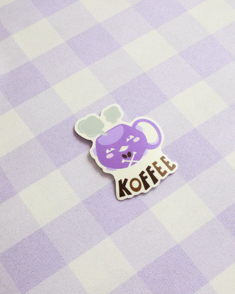 Sticker with a purple character and 'KOFFEE' text on a purple and white checkered background