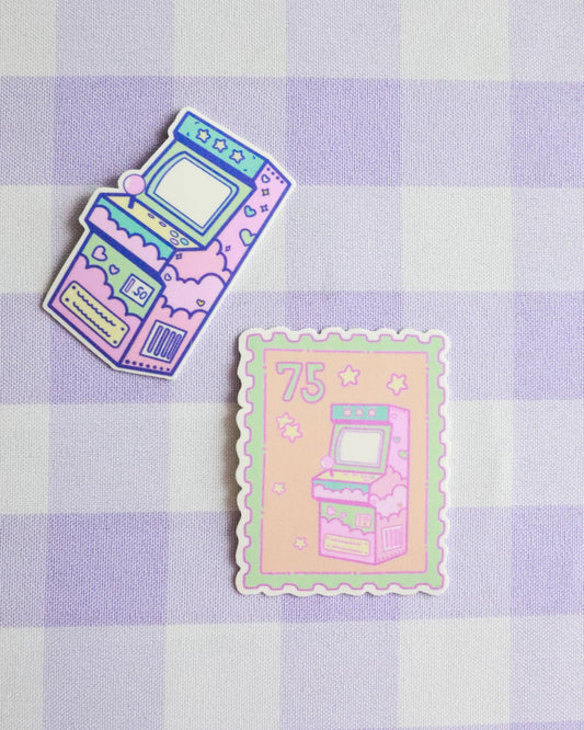 Two pastel-colored sticker designs of vintage arcade machines on a purple checkered background.