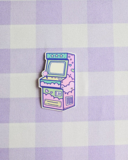 Pastel-colored arcade machine pin on a purple and white checkered background