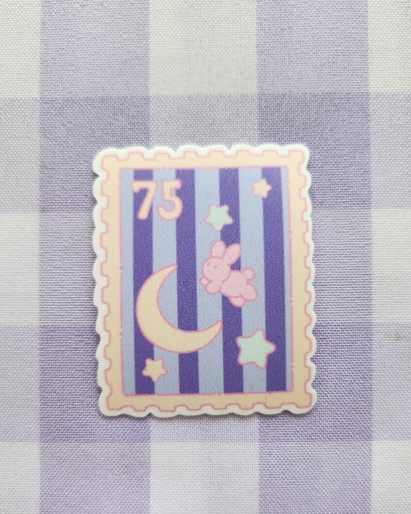 Decorative postage stamp with stars, moon, and number 75 on a checkered fabric background
