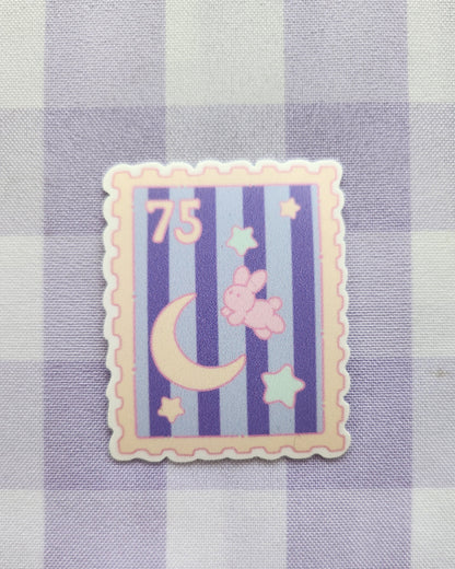 Decorative postage stamp with stars, moon, and number 75 on a checkered fabric background