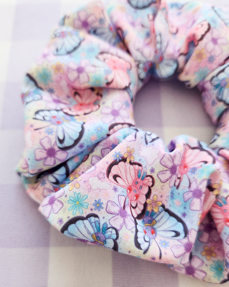 Three colorful scrunchies with floral and cartoon designs on a striped background