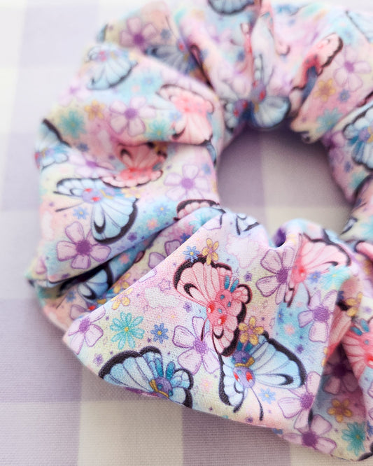 Three colorful scrunchies with floral and cartoon designs on a striped background