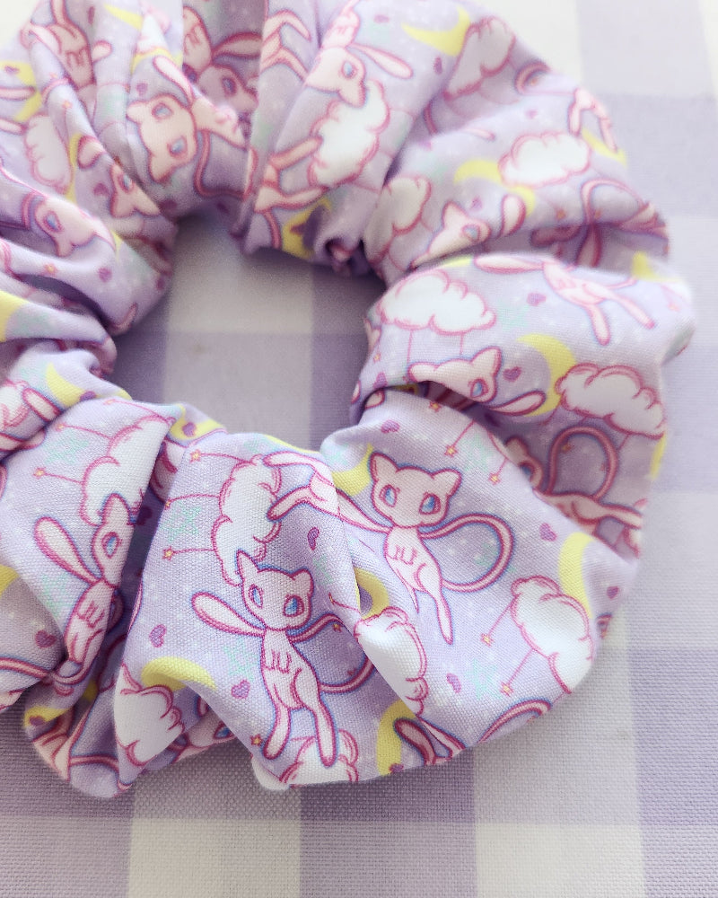 Three pink scrunchies with cartoon designs on a checkered fabric background